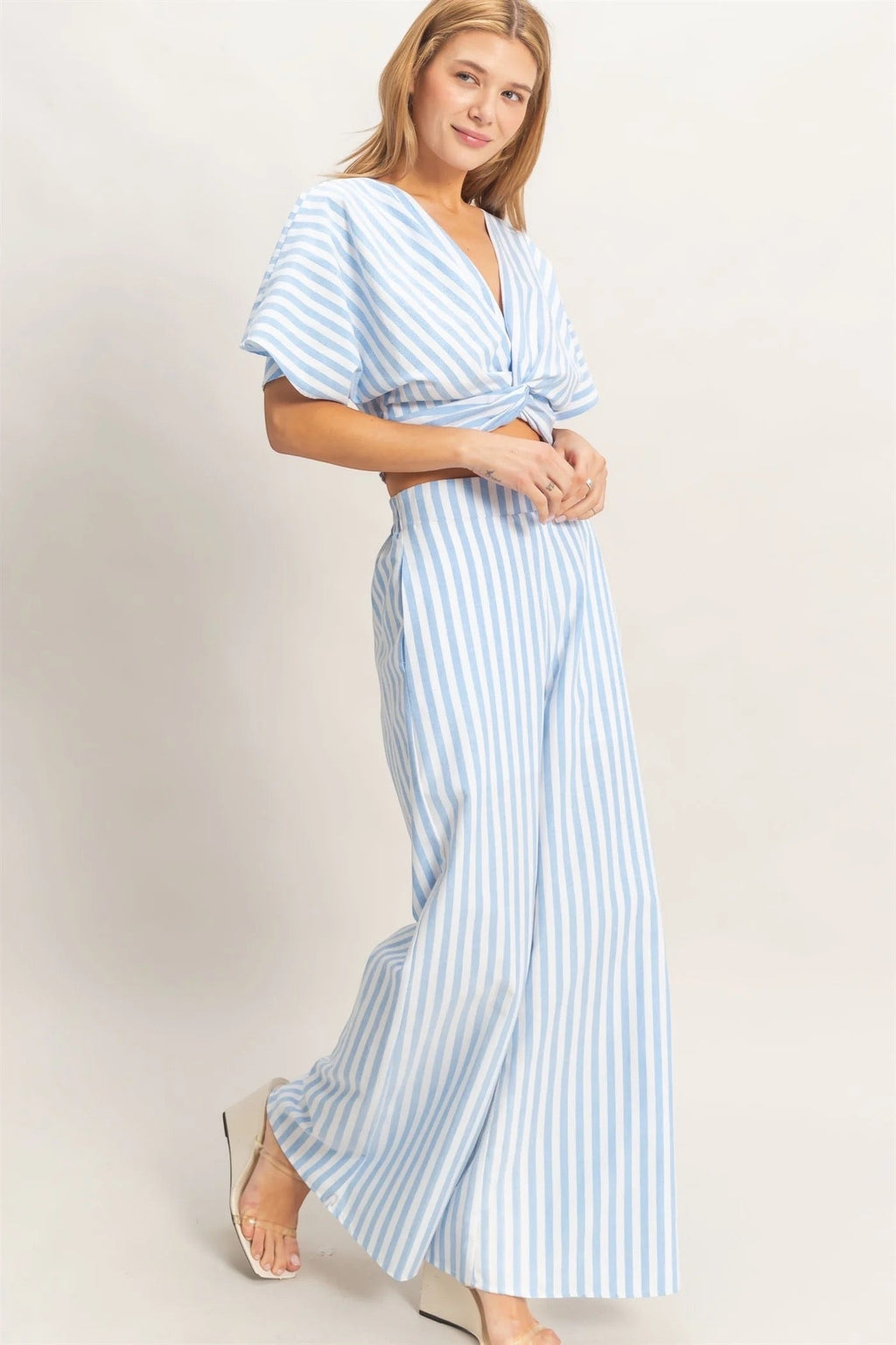 Discover a chic two-piece set featuring a twist front top with a low V-neckline and relaxed short sleeves. Complemented by high-waist wide-leg pants, this ensemble combines a striking striped pattern with a flowing silhouette. Pair with sleek sandals for a polished summer outfit.