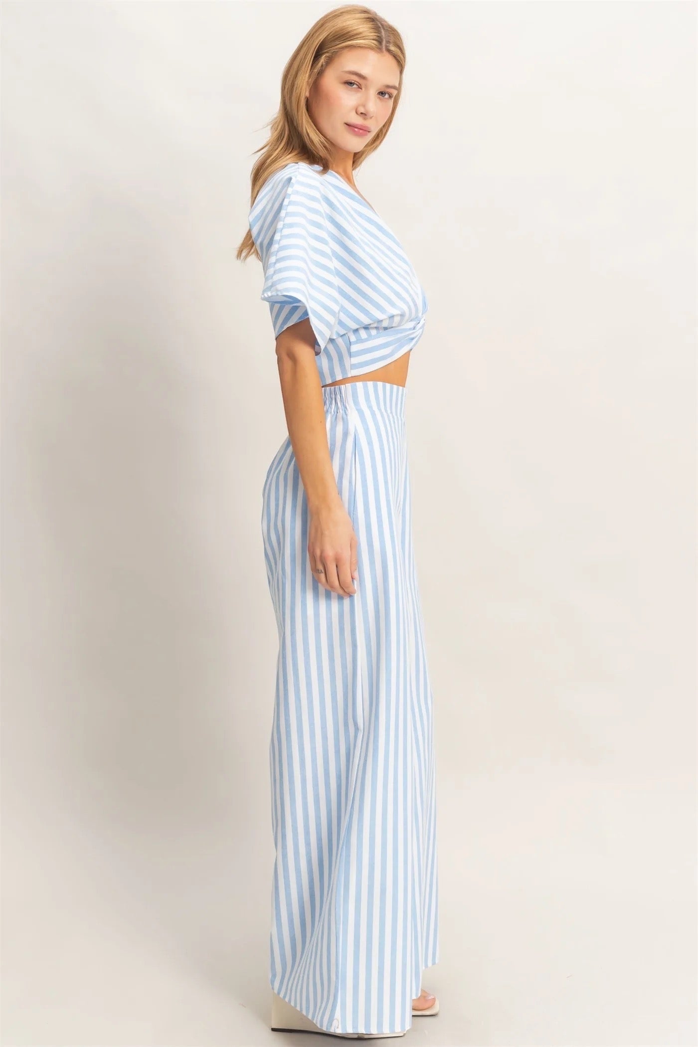 Discover a chic two-piece set featuring a twist front top with a low V-neckline and relaxed short sleeves. Complemented by high-waist wide-leg pants, this ensemble combines a striking striped pattern with a flowing silhouette. Pair with sleek sandals for a polished summer outfit.