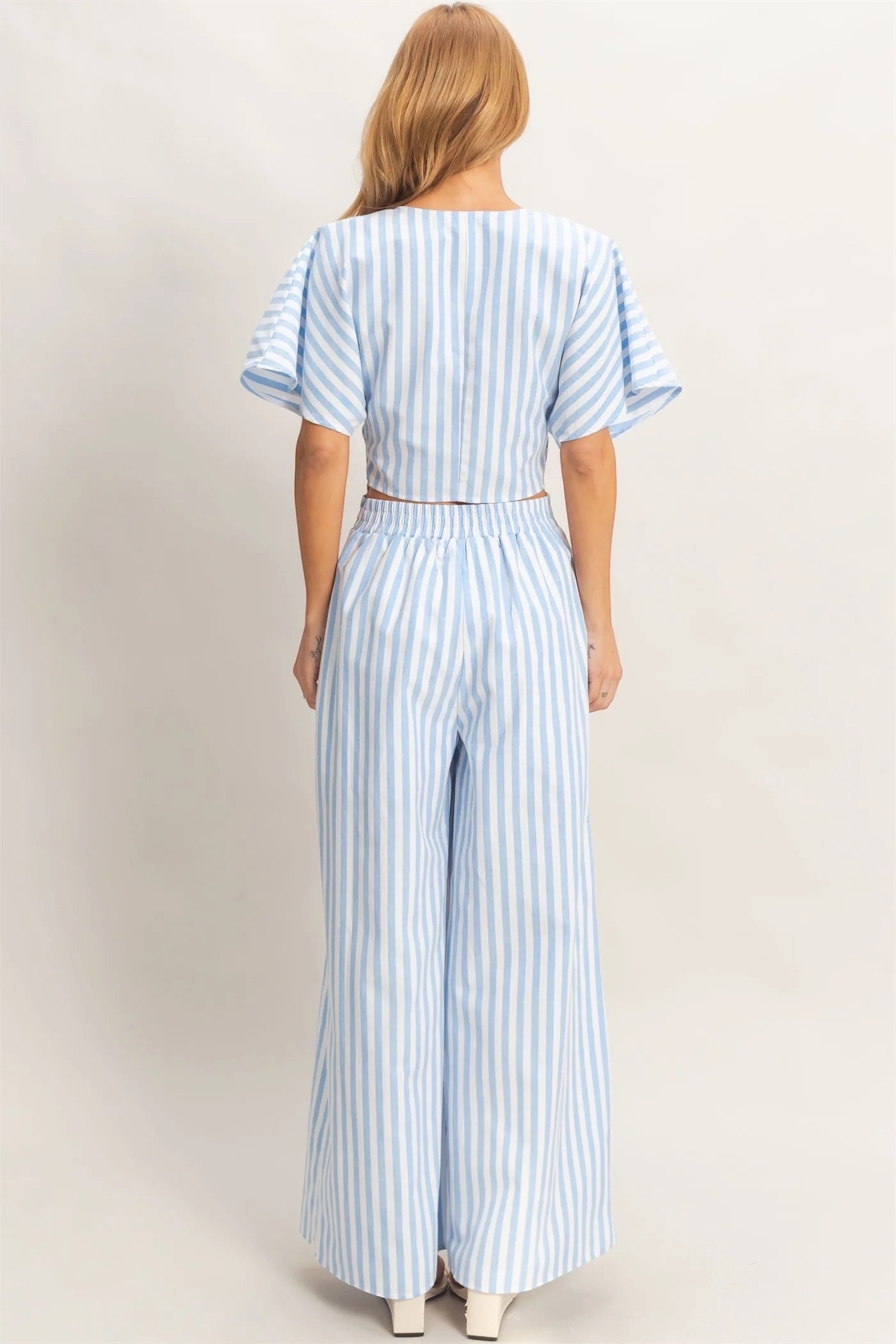Discover a chic two-piece set featuring a twist front top with a low V-neckline and relaxed short sleeves. Complemented by high-waist wide-leg pants, this ensemble combines a striking striped pattern with a flowing silhouette. Pair with sleek sandals for a polished summer outfit.